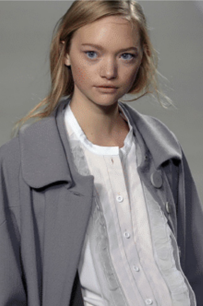 A blonde, white Chloé model wears a white button up shirt and gray peacoat jacket.