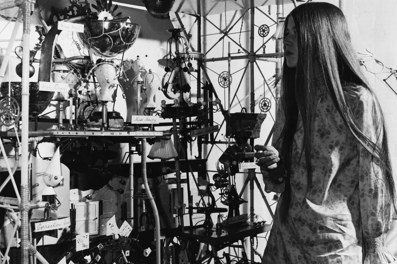 A person with long brown hair stands in front of an installation at the Cybernetics Serendipity exhibition.