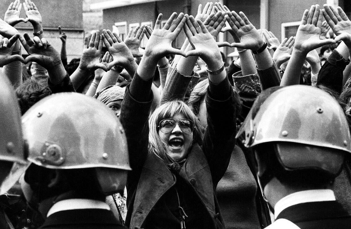 A feminist protester stands amidst a crowd of police.